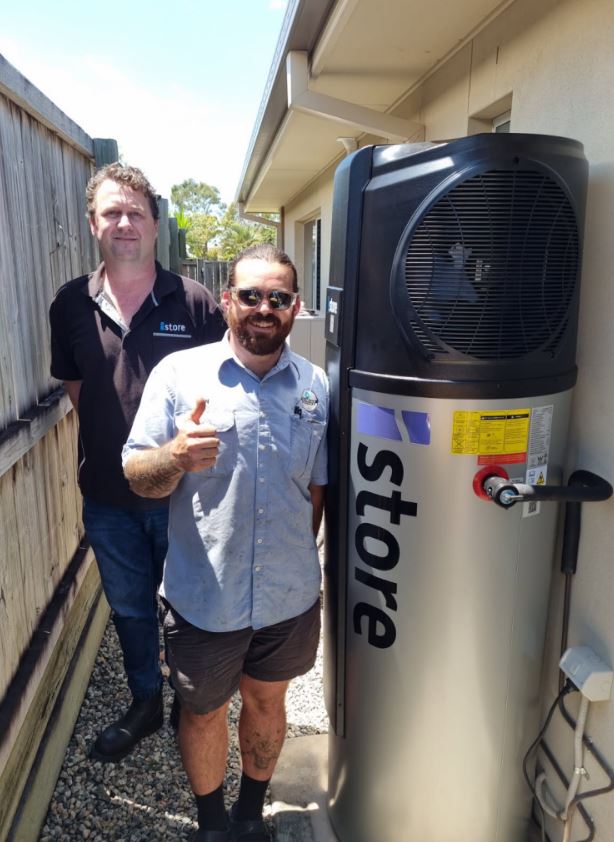 Newly installed iStore heat pump hot water system beside a house, with two men standing next to it