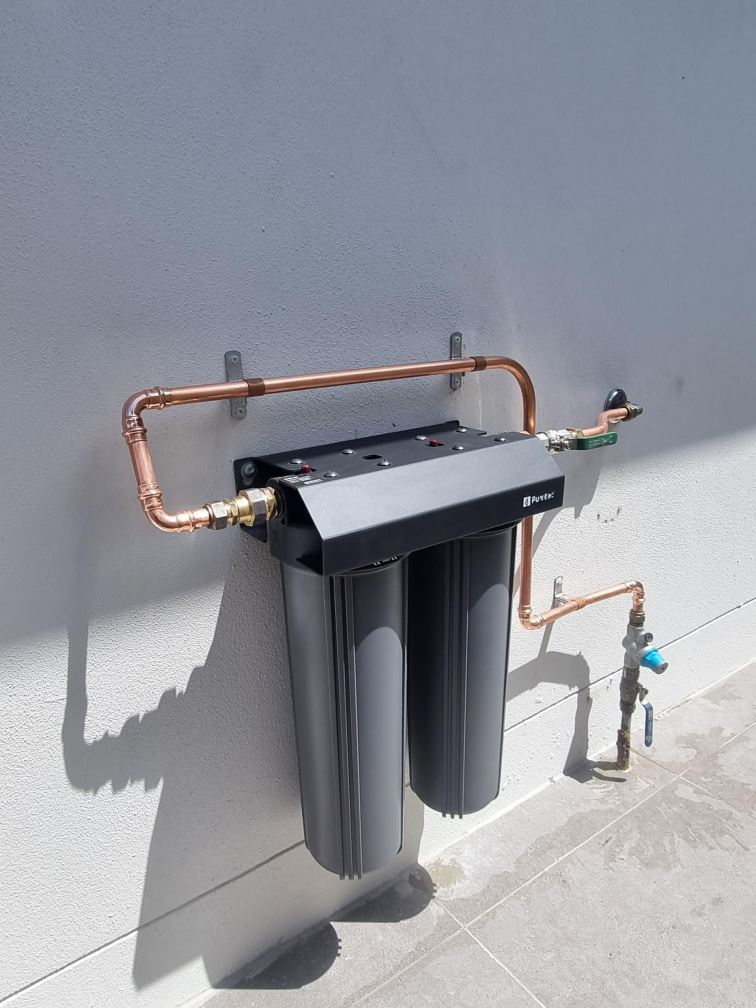 Twin-cartridge PureTec water filter mounted on an outside wall with copper pipework